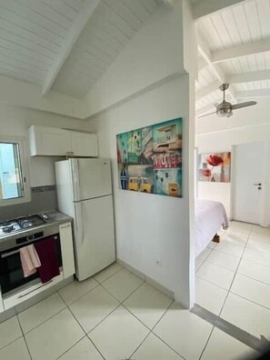 A compact kitchen with a refrigerator, stove, and microwave. There is a painting on the wall and a ceiling fan. - To complete (Grand Case)