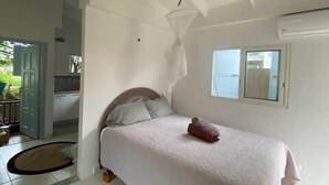 Une chambre à coucher comprenant un lit, un ventilateur de plafond, une fenêtre et une porte donnant sur une autre pièce.