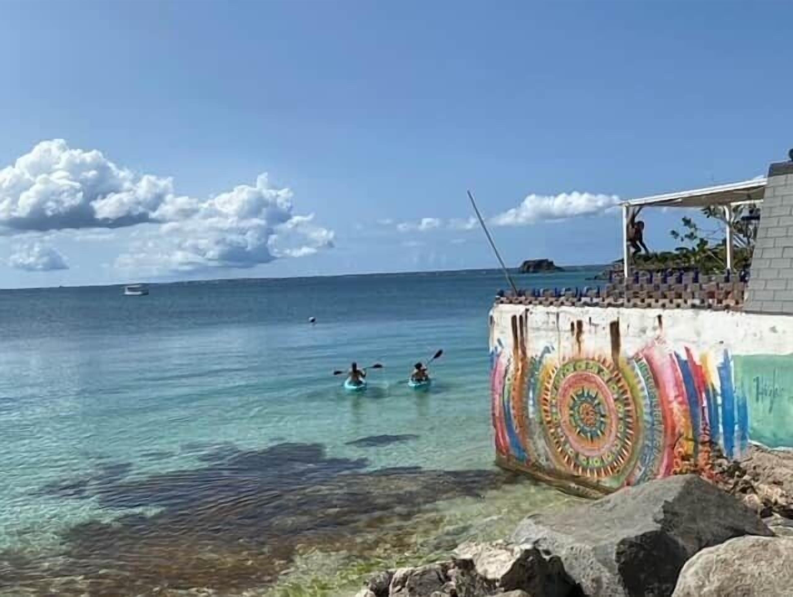 A beach with clear water, a colorful mural on a structure, and two people in the water.