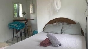 Een bed met een witte spreideken, hoofdbord en een hangend muggengaas.