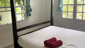 Una cama con dosel, una ventana con cortinas y un par de toallas rojas sobre la cama.