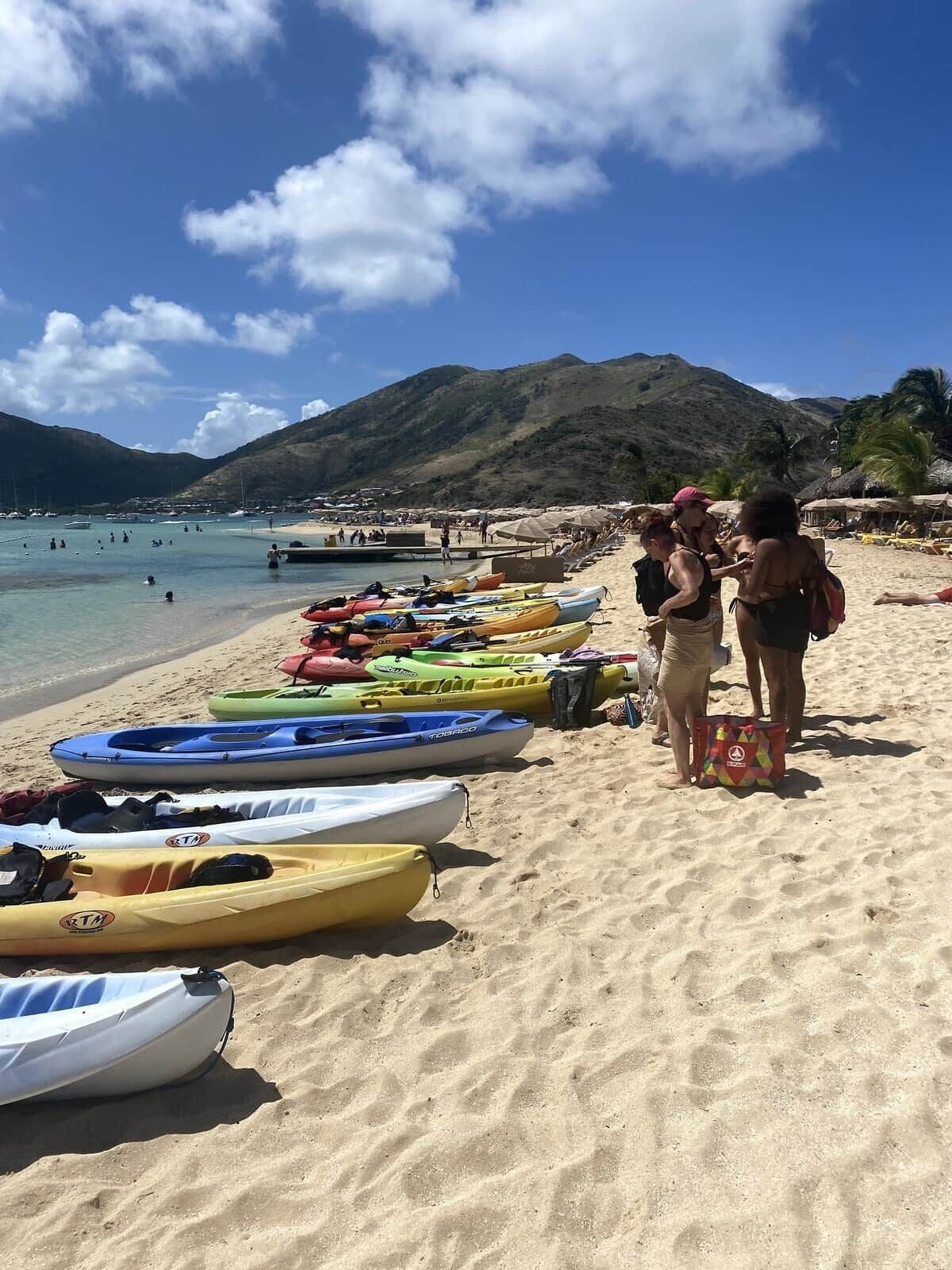 A beach with kayaks lined up and people standing on the sand.