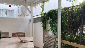 Una terraza de madera al aire libre con una mesa y sillas, rodeada de paredes blancas y un jardín.