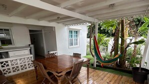 A wooden deck with a dining table and chairs, a hammock, and a view of greenery. - Happy House in Grand Case Beach 1 (Grand Case)
