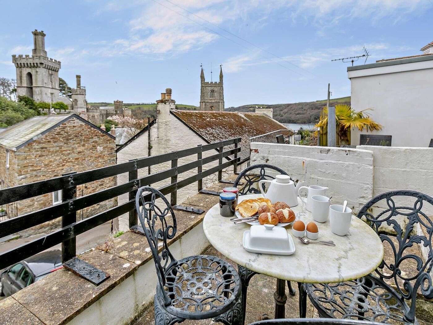 A terrace with a table set for breakfast, overlooking historic buildings and a body of water.