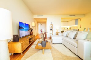 A modern living room with a flat-screen TV, a wooden coffee table, a white sofa, and a kitchen area in the background. - One-bedroom apartment in Bayline, Armação de Pêra, for a maximum of 2 guests. Includes AC, Wi-Fi, equipped kitchen, private parking, pool, spa and gym. Short walk to the beach and promenade. (Armação de Pêra)