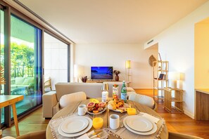 A modern living room with a dining area, a television, and a view through a glass door. - One-bedroom apartment in Bayline, Armação de Pêra, for a maximum of 2 guests. Includes AC, Wi-Fi, equipped kitchen, private parking, pool, spa and gym. Short walk to the beach and promenade. (Armação de Pêra)