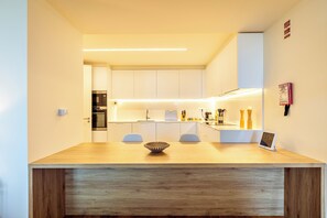 A modern kitchen with white cabinets, a wooden countertop, and a digital clock displaying 11:56. - One-bedroom apartment in Bayline, Armação de Pêra, for a maximum of 2 guests. Includes AC, Wi-Fi, equipped kitchen, private parking, pool, spa and gym. Short walk to the beach and promenade. (Armação de Pêra)