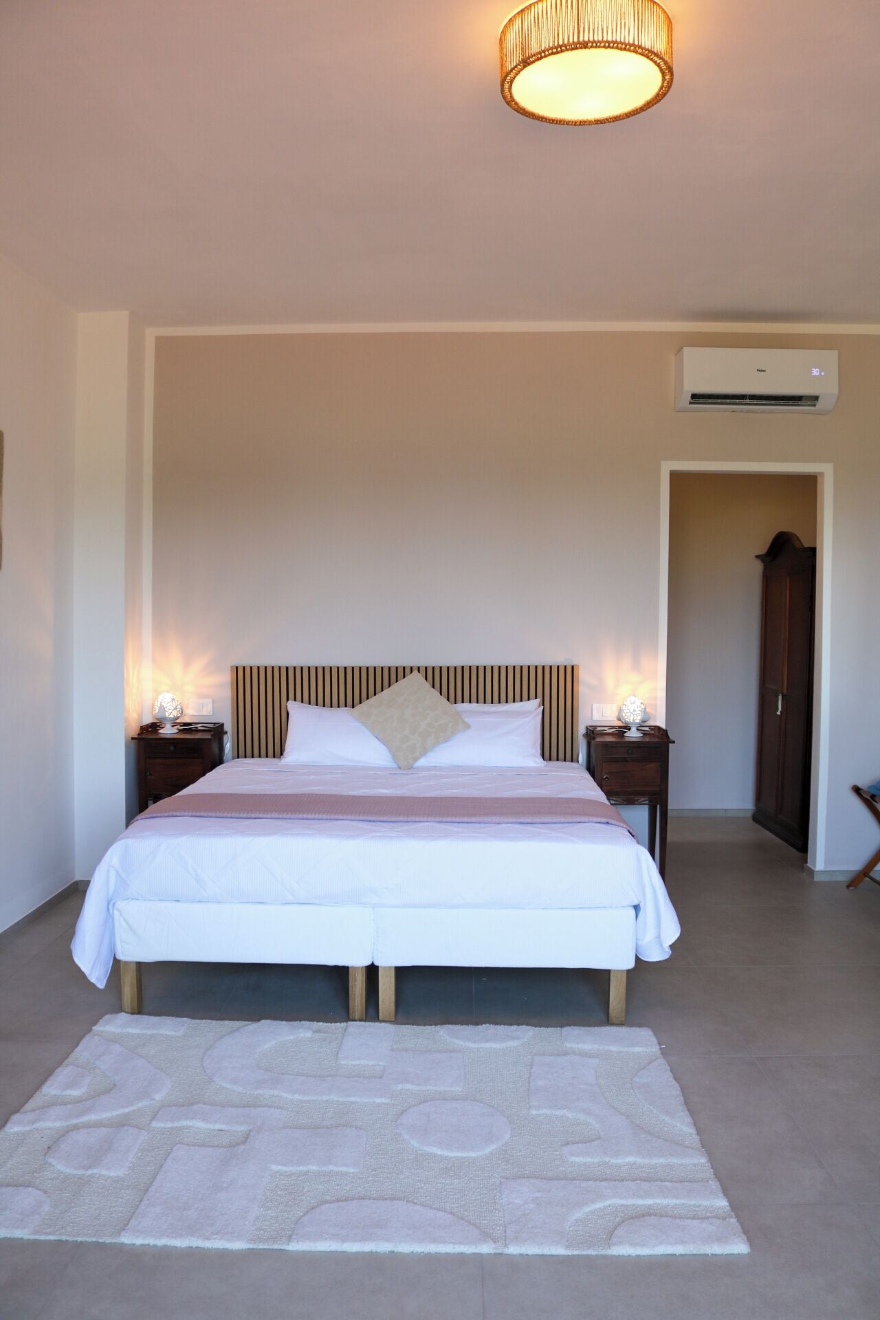 Una camera da letto con un letto, lampade da comodino, un tappeto, un condizionatore d'aria a parete e una porta.