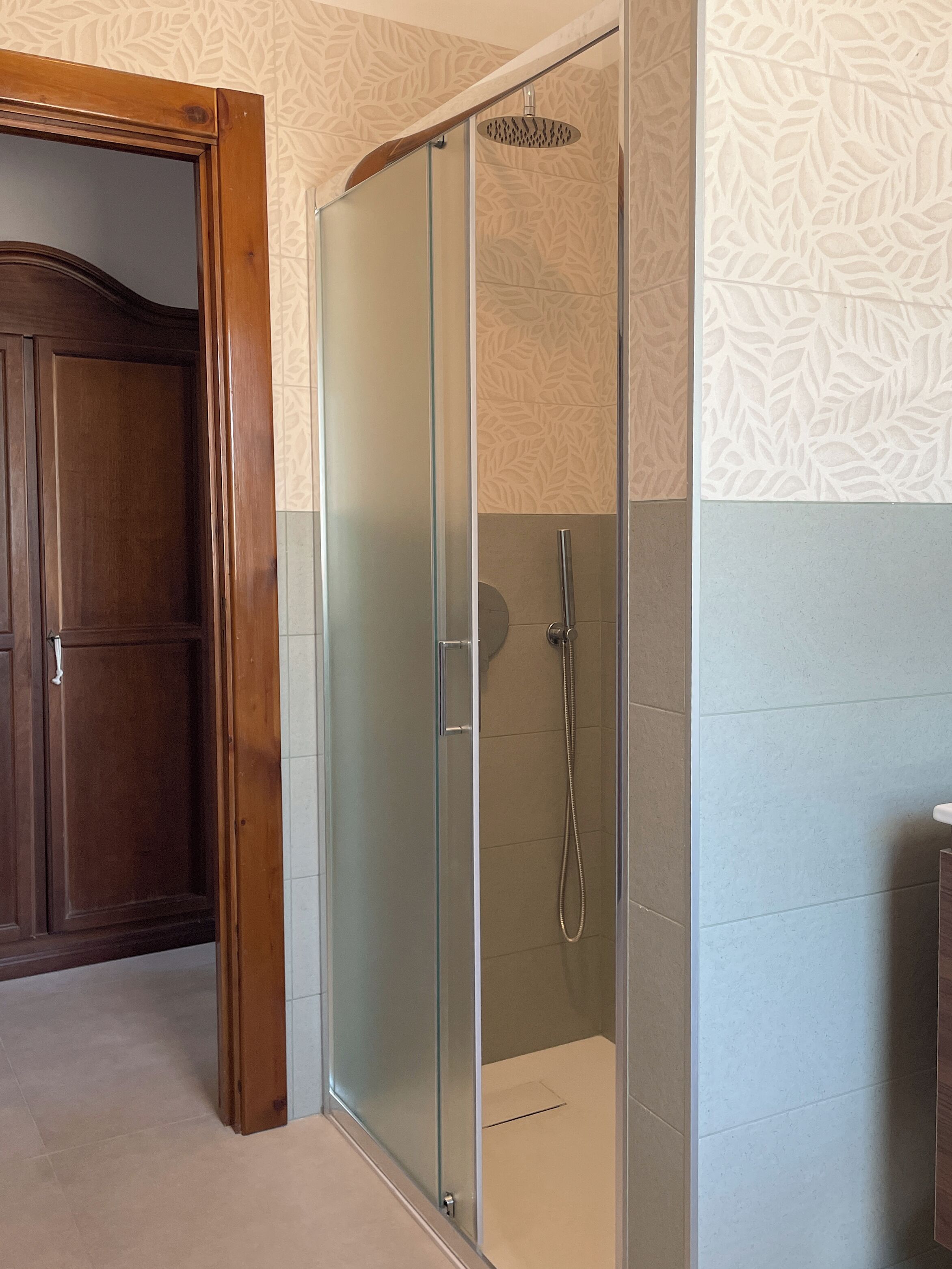 Una doccia vetrata con soffione a mano, una porta in legno e piastrelle a motivi decorativi.