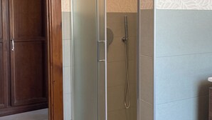 A glass-enclosed shower with a handheld showerhead, a wooden door, and patterned wall tiles. - Room-casa Allegria, Camera Felicità - ad (Parabita)