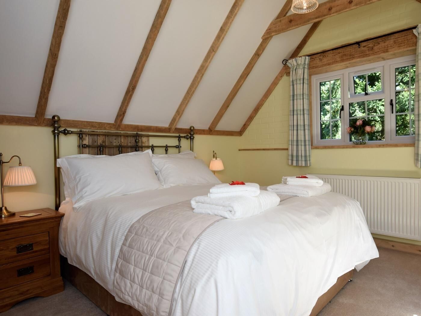 A bedroom with a wooden ceiling, a bed with white bedding, a bedside lamp, and a window with curtains.