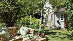Un banc et une table en bois sont installés dans un jardin, avec une maison en arrière-plan.