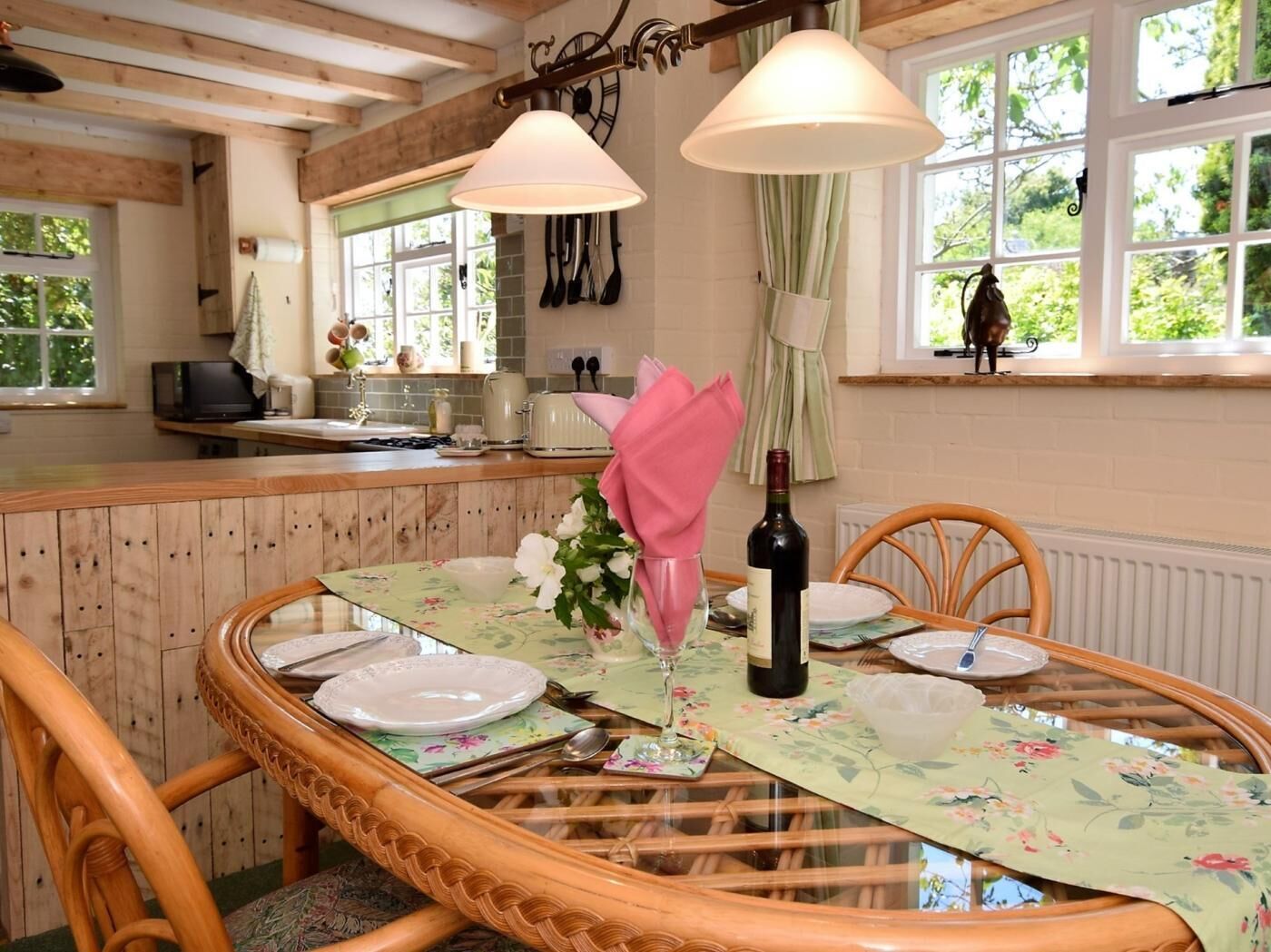A dining area with a round table set for two, a bottle of wine, and a vase of flowers.