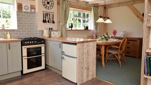 Une cuisine compacte dotée d’un îlot central, de poutres en bois, d’une horloge et d’un coin repas avec une table et des chaises.