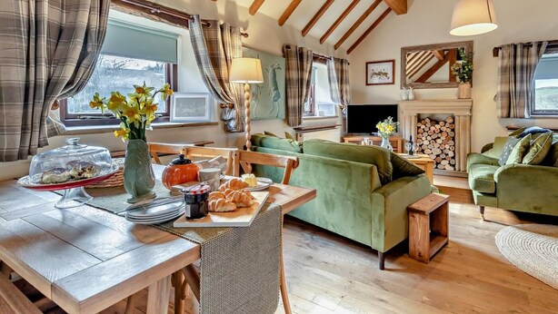 Een gezellige woonkamer met een houten plafond, een open haard, een groene bank en een eethoek met een tafel gedekt voor het ontbijt.