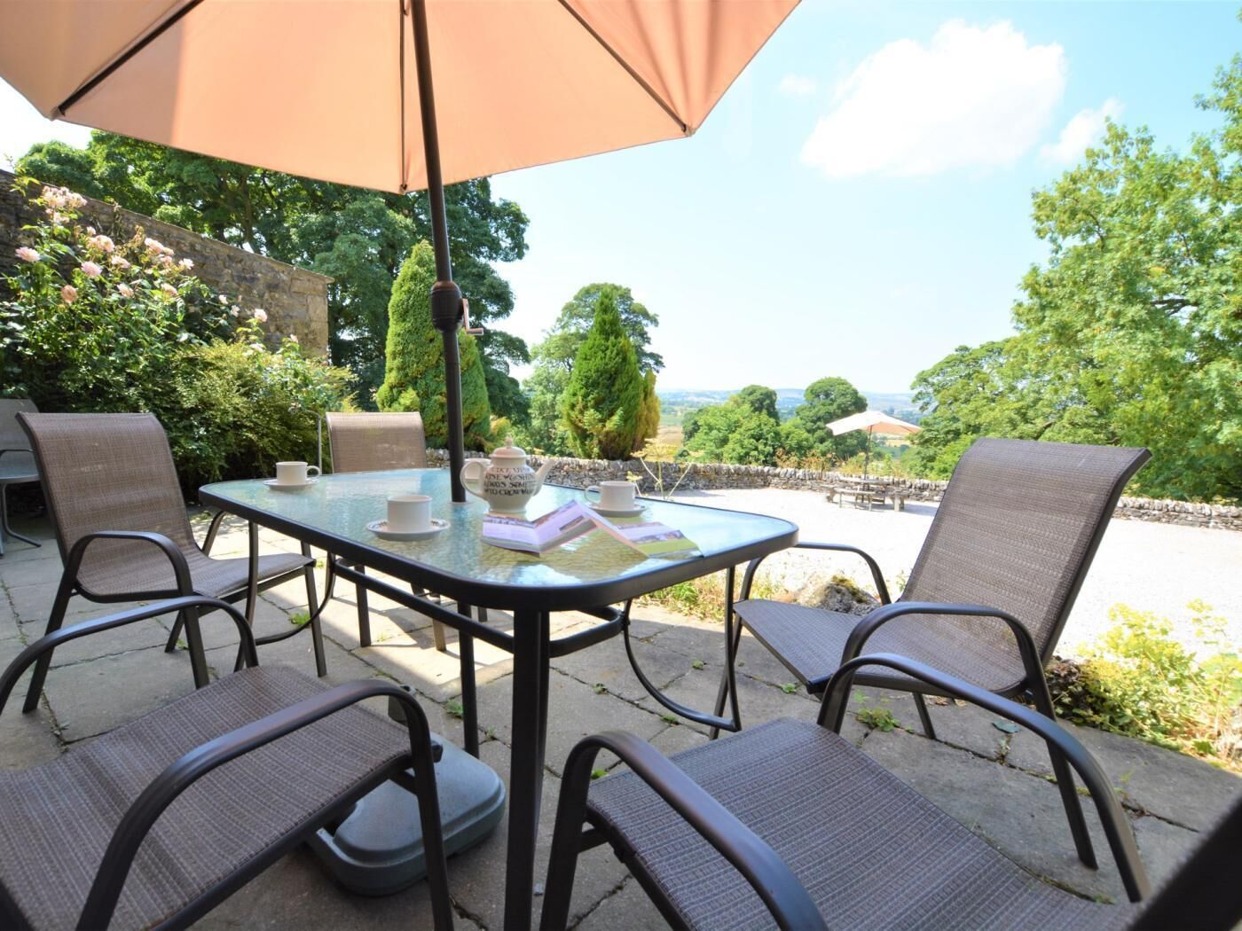 Una terrazza esterna con un tavolo in vetro, quattro sedie e un ombrellone grande.