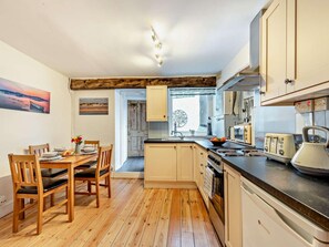 Une cuisine de taille réduite, dotée d’un plancher en bois, d’une table à manger avec des chaises et d’appareils électroménagers de base.