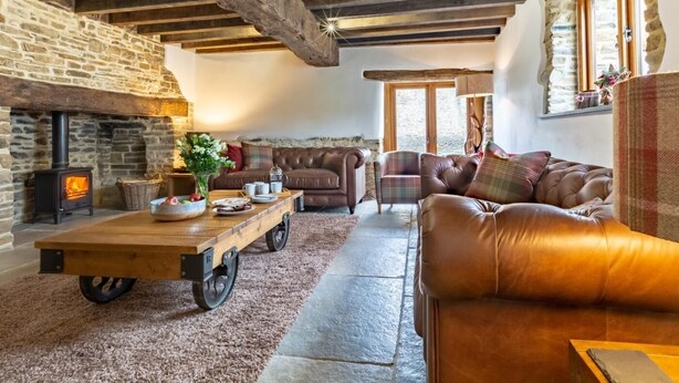 Un interior rústico con vigas de madera a la vista, una chimenea de piedra, sofás de cuero y una mesa de centro de madera.