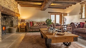 Un salón acogedor con chimenea de piedra, sofás de cuero, una mesa de centro de madera y techo rústico.