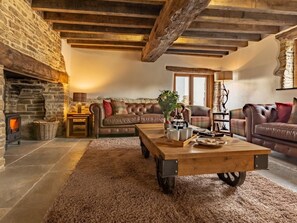 A cozy living room with a stone fireplace, leather sofas, a wooden coffee table, and a rustic ceiling. - 4 Bed in Braunton (oc-62949) (Croyde)