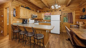 A wooden cabin-style kitchen with a bar area, bar stools, a refrigerator, and a sink. - Escape to Friendly Bear Cabin, a welcoming three-bedroom retreat in Sevierville (Sevierville)