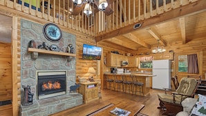 A log cabin interior with a stone fireplace, wooden ceiling beams, a kitchen area, and a cozy seating arrangement. - Escape to Friendly Bear Cabin, a welcoming three-bedroom retreat in Sevierville (Sevierville)