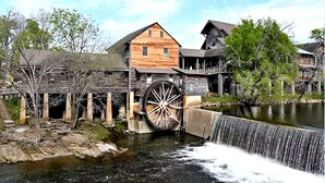 A historic wooden building with a large water wheel and a wooden bridge over a river. - Escape to Friendly Bear Cabin, a welcoming three-bedroom retreat in Sevierville (Sevierville)