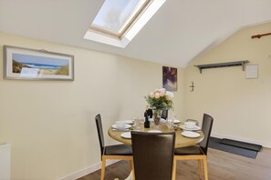 A dining room with a round table, chairs, a vase of flowers, and a skylight. - 2 Bed in Beaminster (oc-63047) (Littlewindsor)