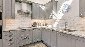 A modern kitchen with grey cabinets, a white countertop, a built-in oven, a sink, and a clock on the wall. - 2 Bed in Bideford (oc-62964) (Appledore)