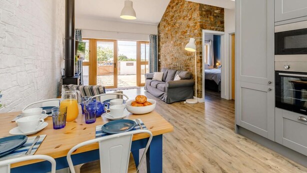 A modern kitchen with grey cabinets, a wooden dining table, and a stone accent wall. - 2 Bed in Bideford (oc-62964) (Appledore)