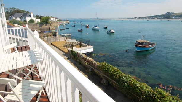 Vista sulla costa con barche ormeggiate, un edificio bianco con un balcone e cielo sereno.
