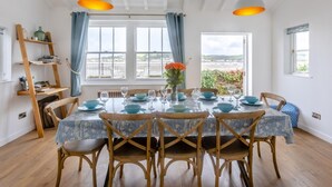 Zona pranzo con tavolo apparecchiato per quattro, sedie in legno, vista panoramica attraverso ampie finestre e tovaglia con decorazioni blu e bianche.