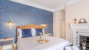 Una camera da letto ordinata con un letto, comodini, un caminetto e una parete con un motivo blu.