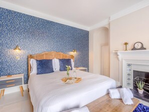 Ein aufgeräumtes Schlafzimmer mit einem Bett, Nachttischen, einem Kamin und einer Wand mit blauem Muster.