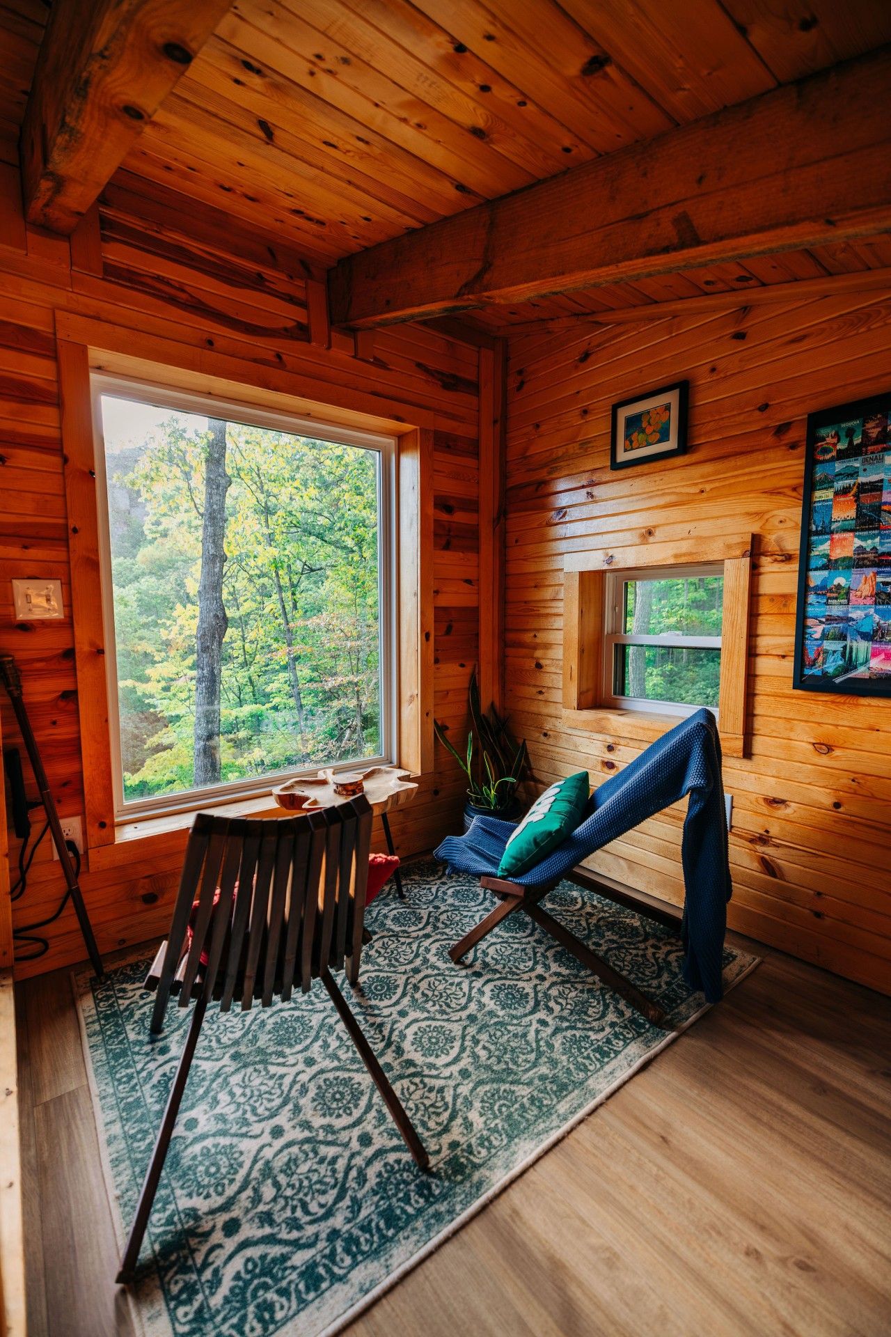 A cabin interior with a large window, a small table, a chair, a rug, and a framed map on the wall.