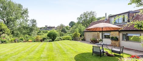 A well-maintained lawn, a patio with outdoor furniture, and a stone building with a tiled roof.