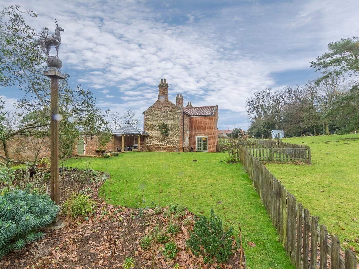 A brick house with a green door, a fenced yard, and a lamp post.