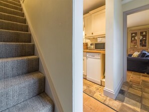 Eine Treppe führt zu einer Küche mit Geschirrspüler und Mikrowelle, einem Essbereich mit einem dunkelgrauen Sofa und einem gefliesten Boden.