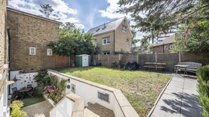 Un jardin à l’arrière d’une maison, avec une terrasse, un petit abri de jardin et une clôture en bois.