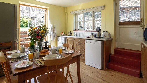 Een compacte keuken met een eethoek, houten vloeren, een wasmachine en een trap naar een deur.