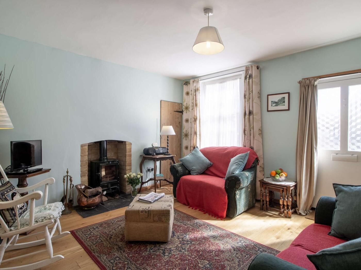 Ein Wohnzimmer mit Kamin, Fernseher, Schaukelstuhl und einem roten Sofa.