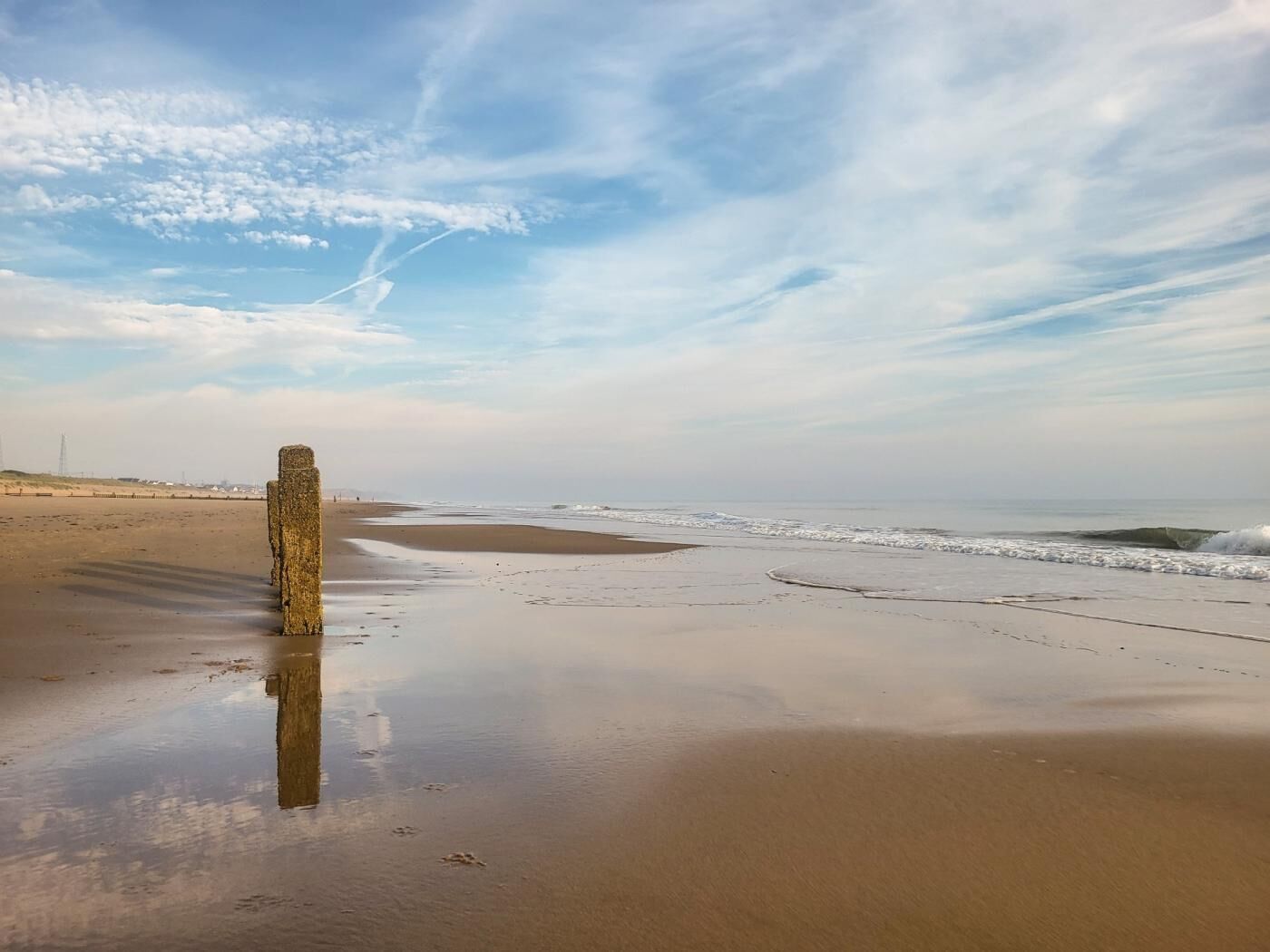 A beach with a solitary pillar, calm waves, and a clear sky.