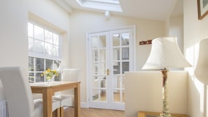 Une pièce comprenant une table à manger en bois, des chaises blanches, une lampe de table en verre et une porte donnant sur une autre pièce.