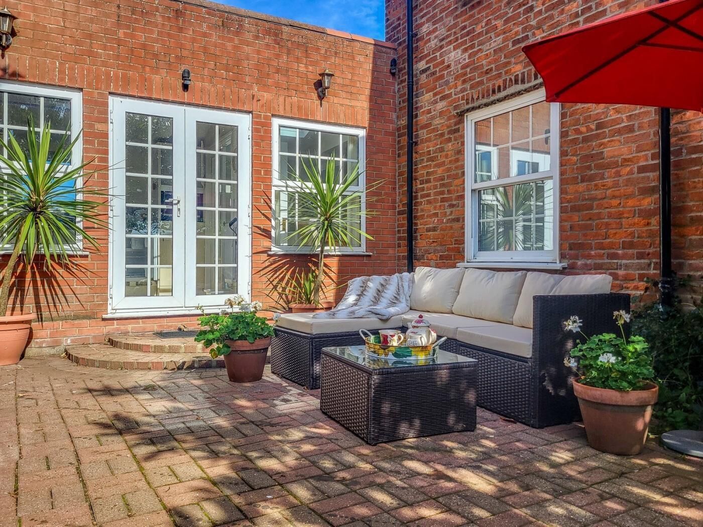 A brick building with large windows, a patio area with a sofa and a coffee table, and potted plants.