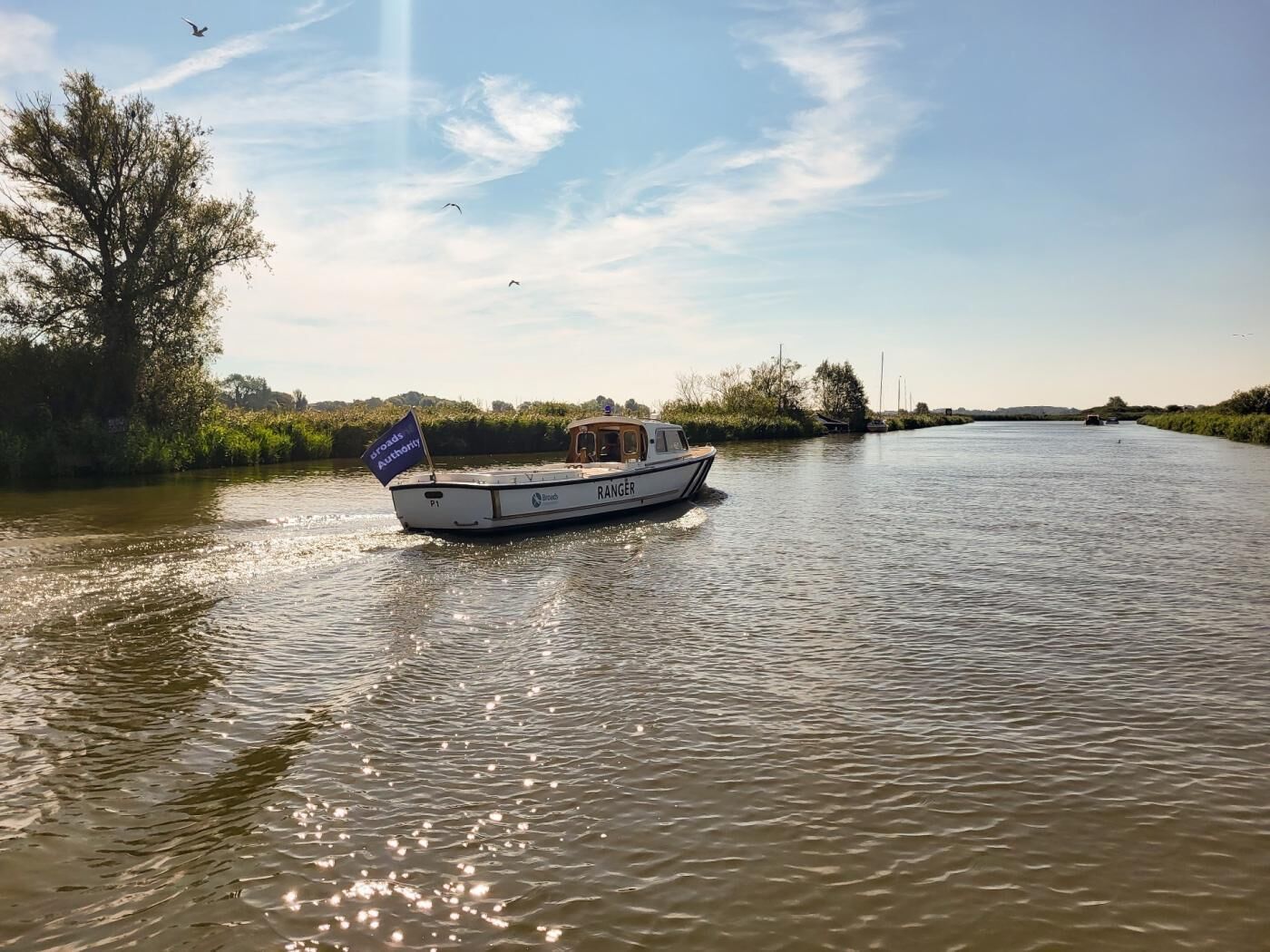 A boat named 'RANGER' on a river with a clear sky and vegetation on the banks.