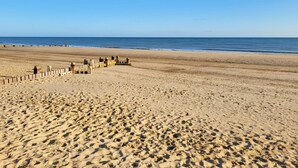 Une vaste plage de sable fin parsemée d’empreintes, une structure en bois et un ciel bleu azur.