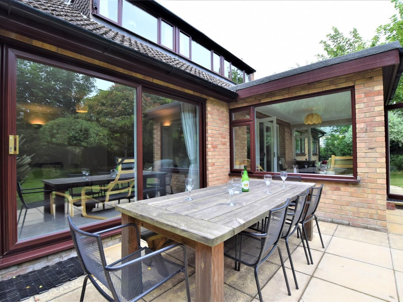 Un patio con mesa y sillas de madera, puertas correderas de vidrio y fachada de ladrillo.