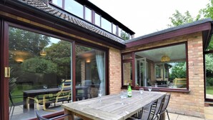 En terrasse med et træbord og stole, store skydedøre af glas og en murstensfacade.