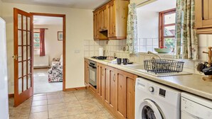 Una cucina con mobili in legno, una lavatrice e una finestra con tende.